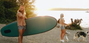 A couple with a husky enjoy paddleboarding on a sunny beach at sunset.